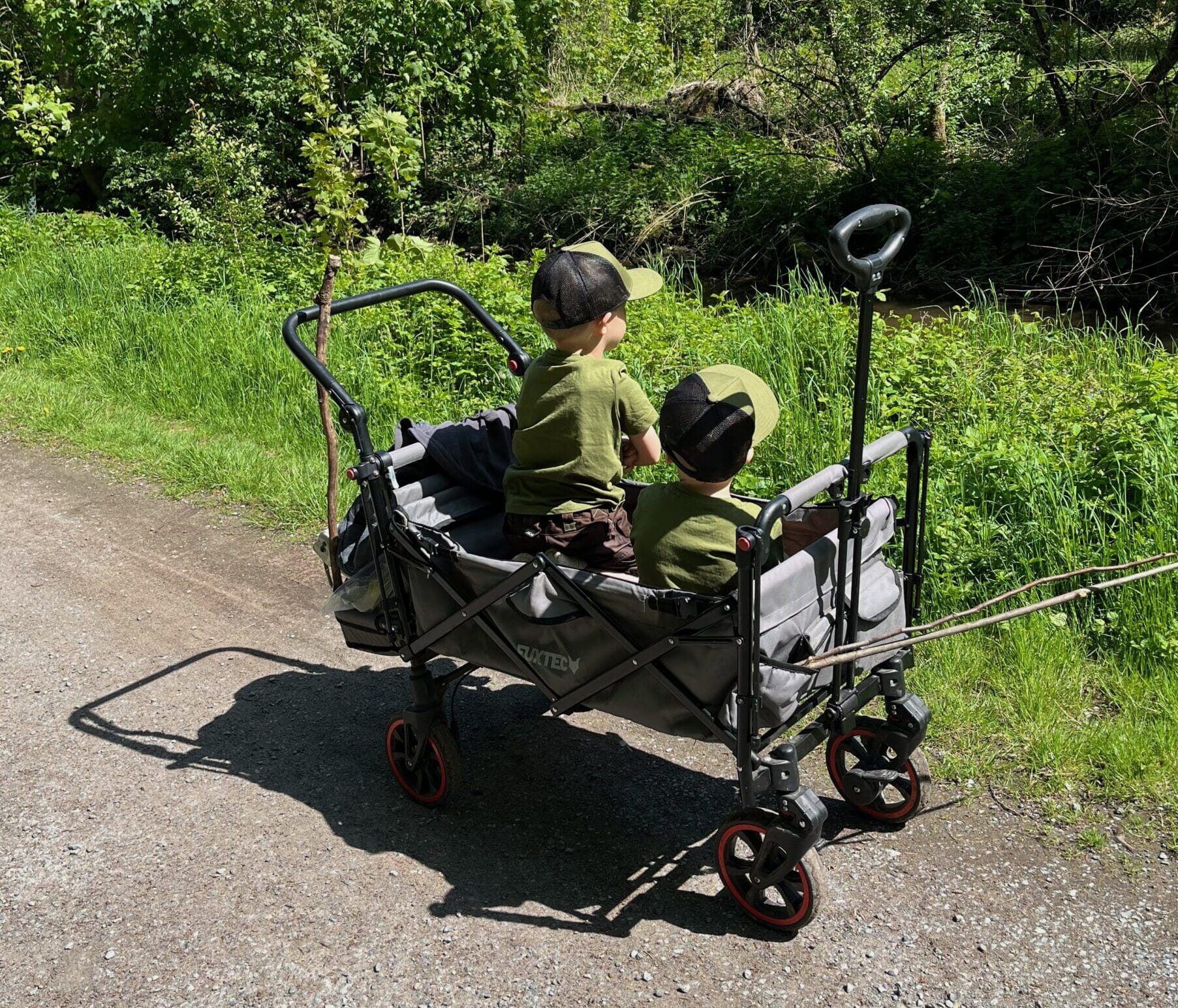 Zwei Kinder sitzen im klappbaren Bollerwagen auf einem Feldweg