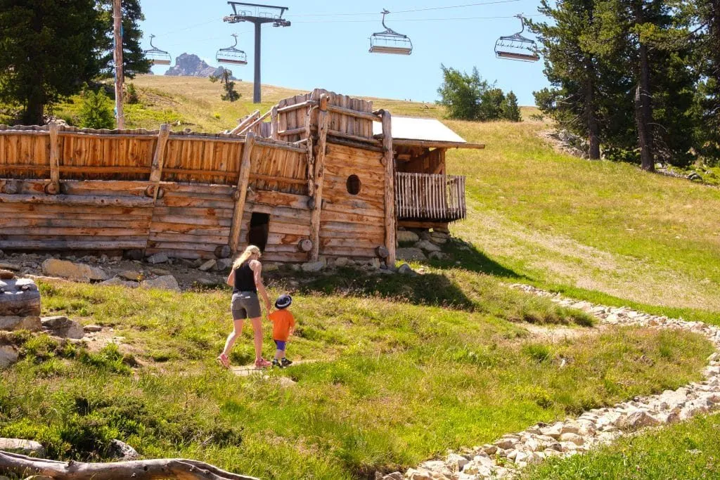 Mutter und Kind laufen über die Almwiese zu einer Holzhütte