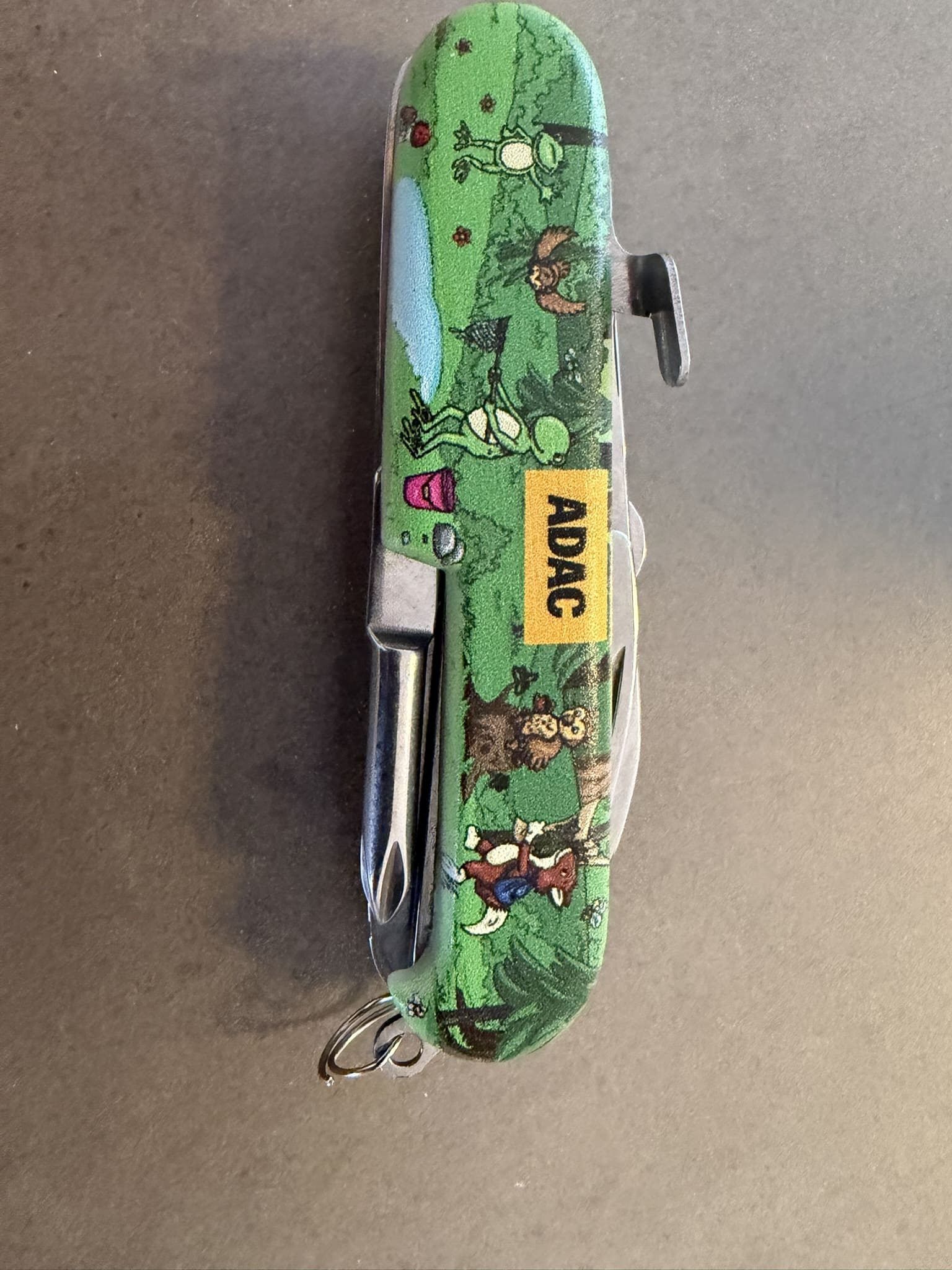 Grünes Kindertaschenmesser mit Waldtier-Motiv und ADAC-Logo auf grauem Grund